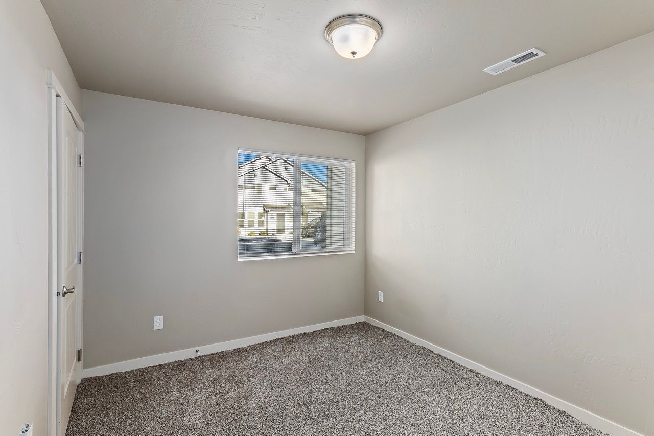 Empty apartment bedroom with beige walls, a window with blinds, and carpet.