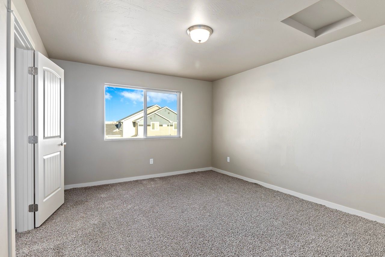Empty beige-carpeted bedroom with a window and interior door.