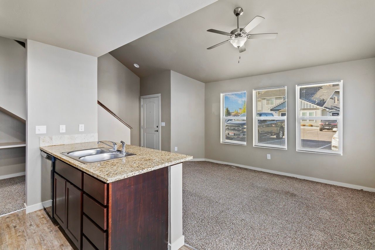 Open-concept kitchen and living area with a granite island, sink, and three windows.