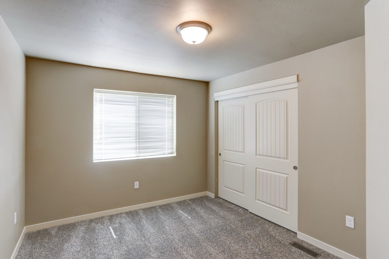 Bedroom with beige walls, plush carpet, a window with blinds, and a double sliding closet.