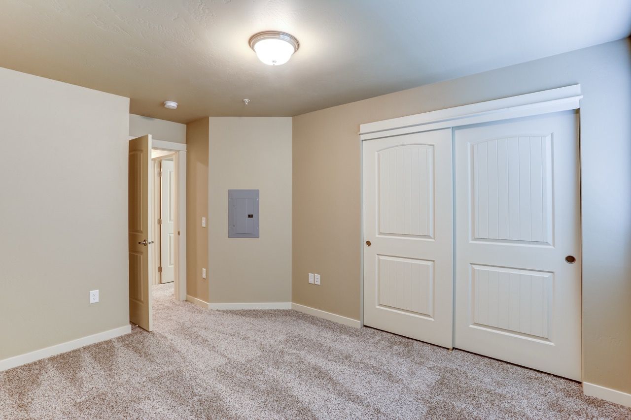 Vacant beige bedroom with carpet, a double sliding-door closet, and a ceiling light.
