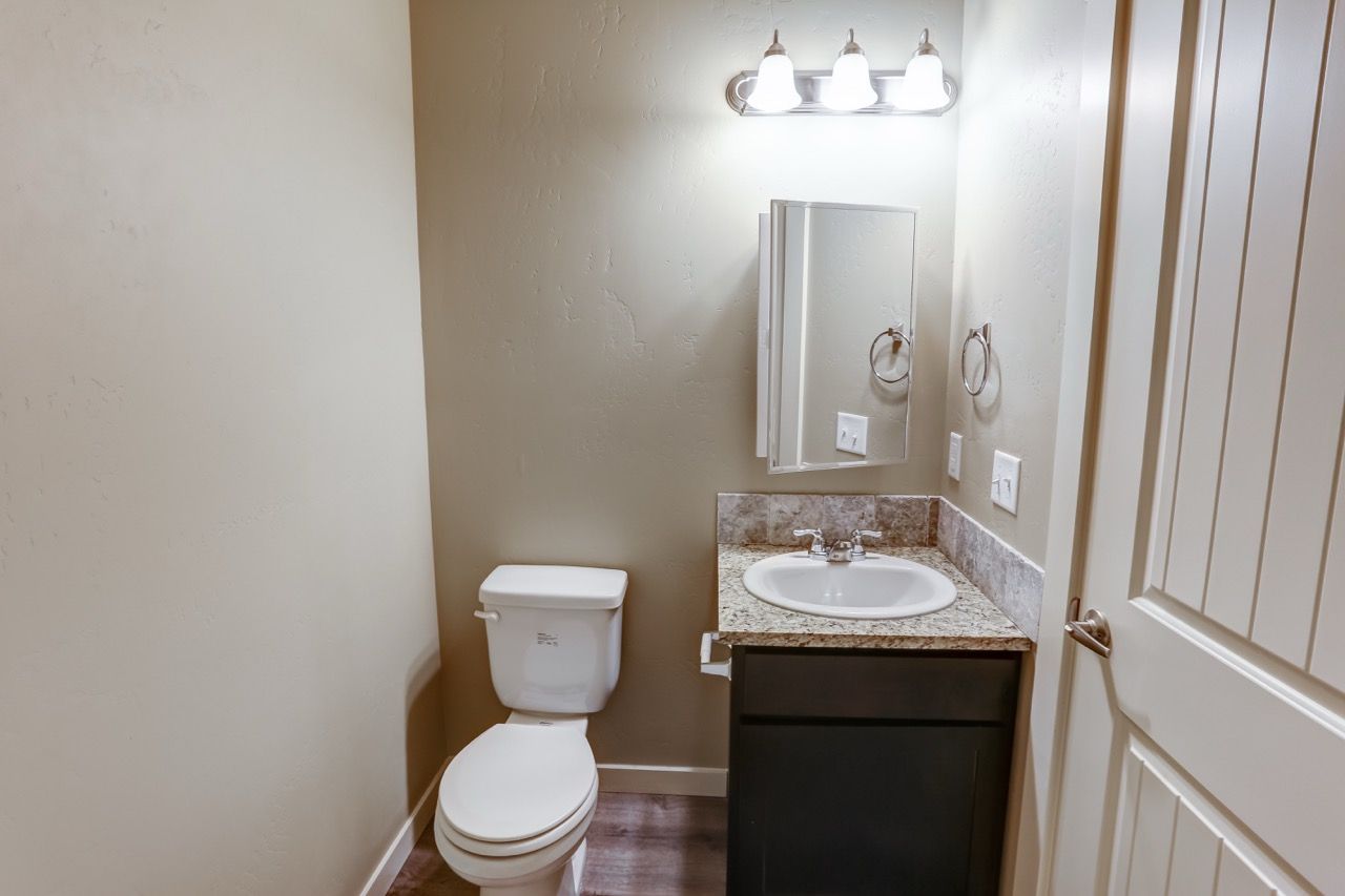 Bathroom in an apartment unit with a vanity, granite countertop, mirror, towel rings, and toilet.