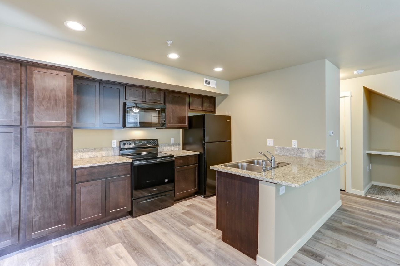 Modern apartment kitchen with dark wood cabinets, granite countertops, and an island.