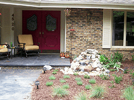 Front porch with burgundy double doors, stone wall, seating, and a landscaped rock garden.