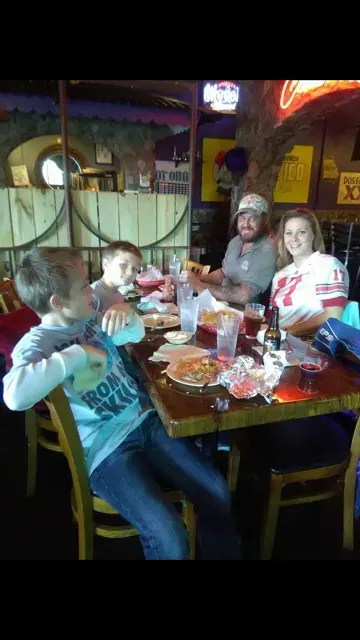 Four people seated at a restaurant table, smiling and raising drinks in a dimly lit bar.