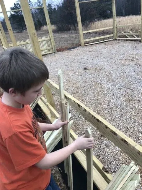Child in an orange shirt holding a wooden railing at an outdoor deck or playground platform