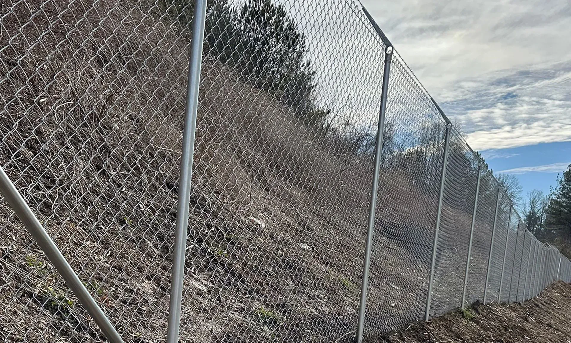 Chain-link fence along a steep rocky hillside under a blue sky