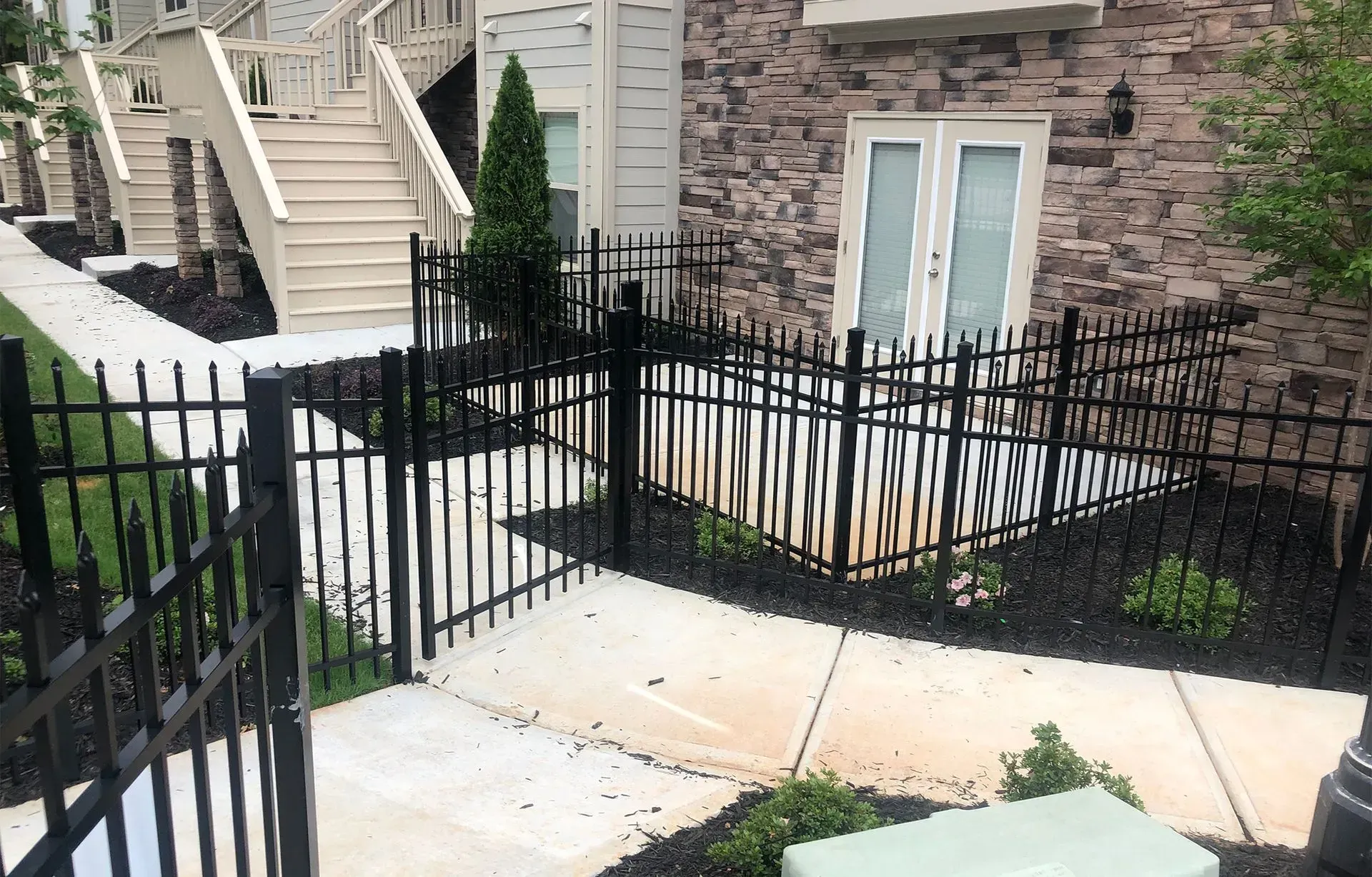 Black wrought-iron fence around a small patio beside brick townhouse stairs and white French doors