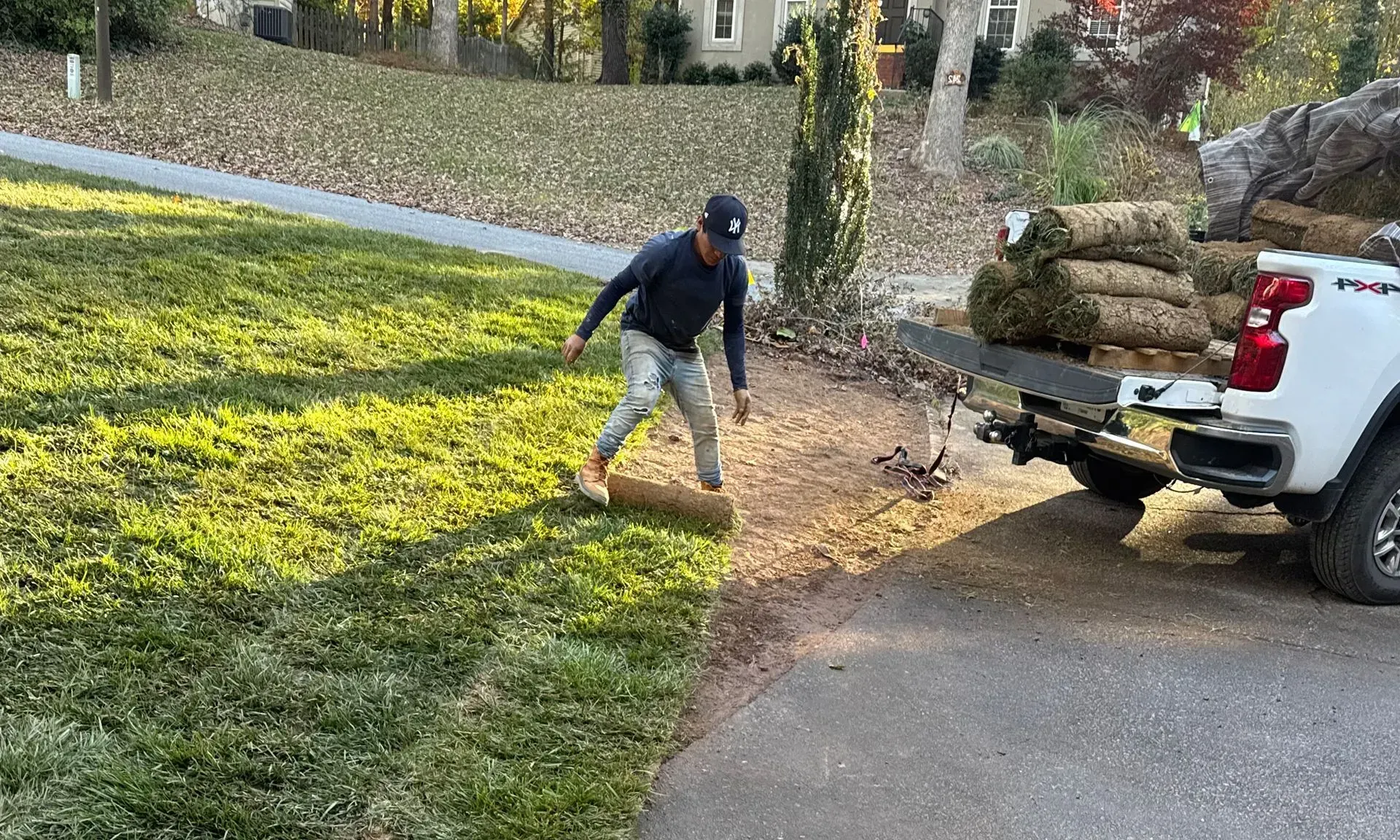 Person raking leaves beside a white truck loaded with bags in a yard by the road