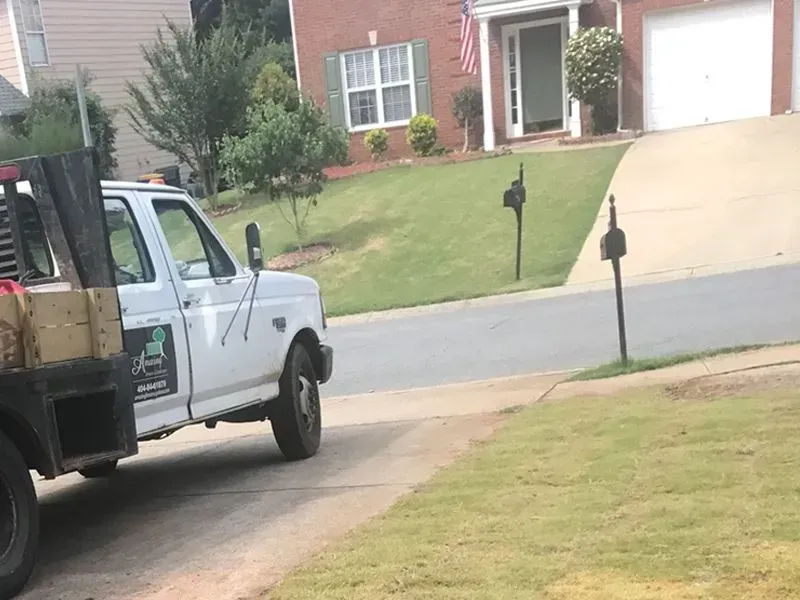 White pickup truck parked in a suburban driveway beside a brick house and green lawn