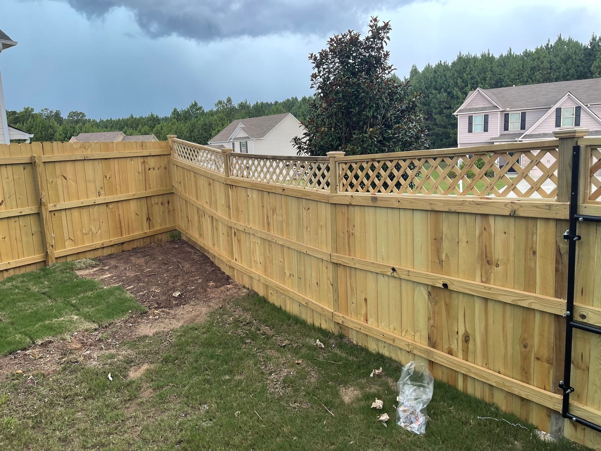 Wooden fenced backyard with lattice top, grass, and a cloudy sky over neighboring houses
