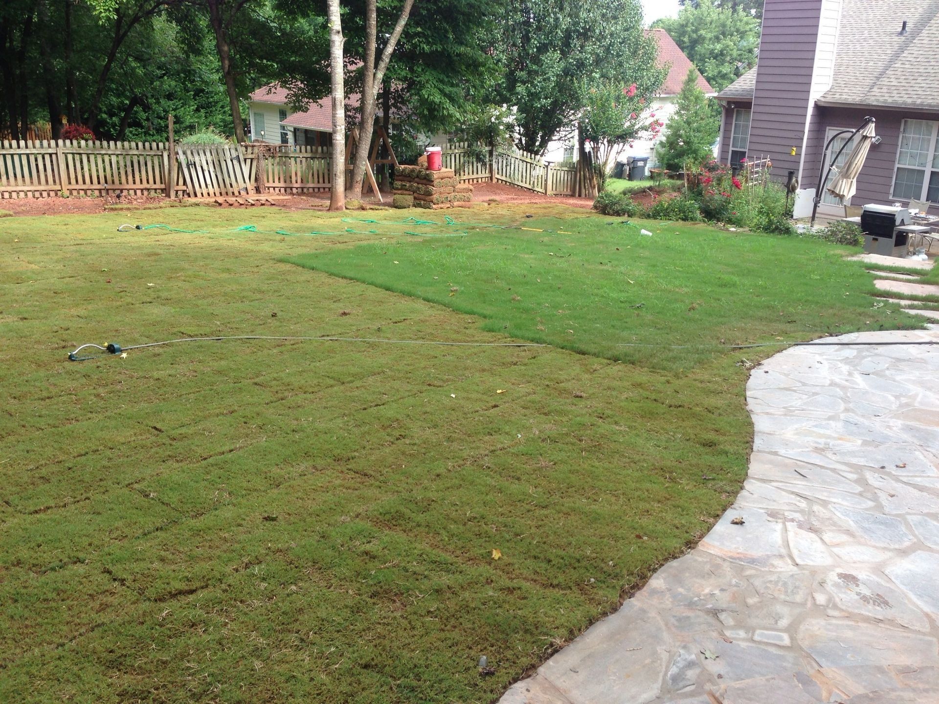 Backyard lawn with a stone patio, trees, and a wooden fence in the background
