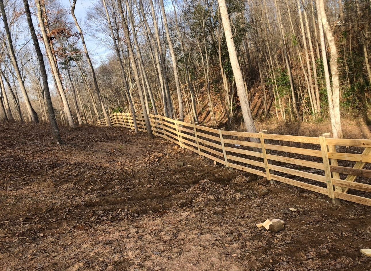 Wooded hillside with leafless trees and a long wooden fence along the right side.
