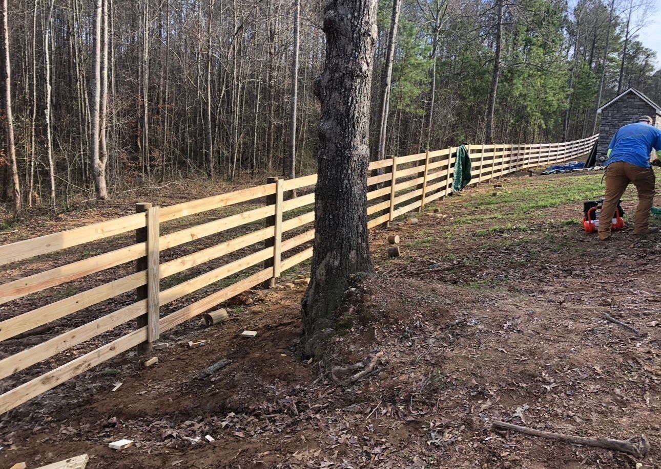 Person installing a light wood fence along a wooded yard trail