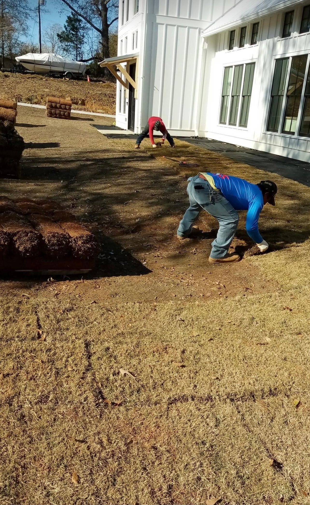 Workers raking leaves beside a white house on a sunny day