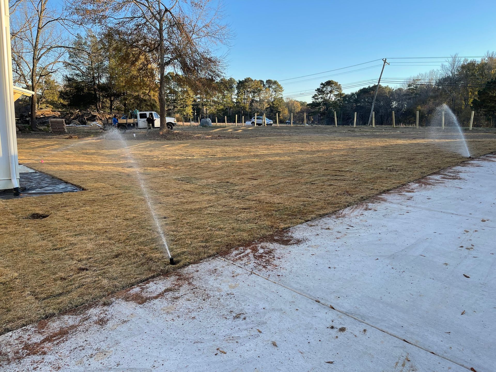 Sprinklers watering a dry grass field beside a concrete path under a clear blue sky