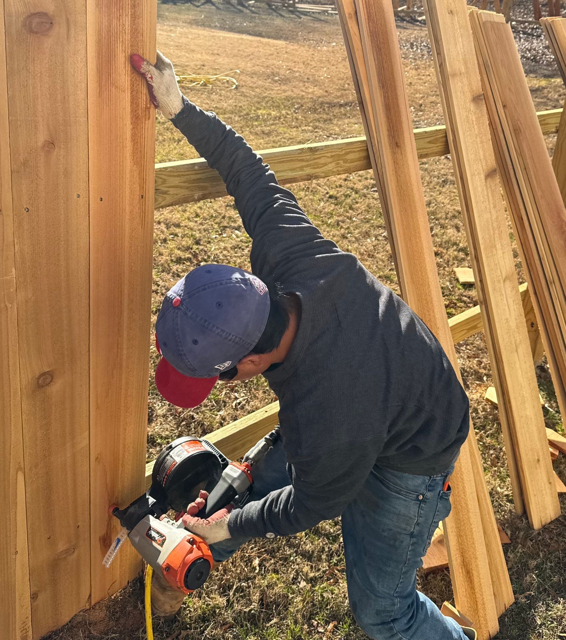 Person using a drill to install vertical wooden boards on a fence outdoors