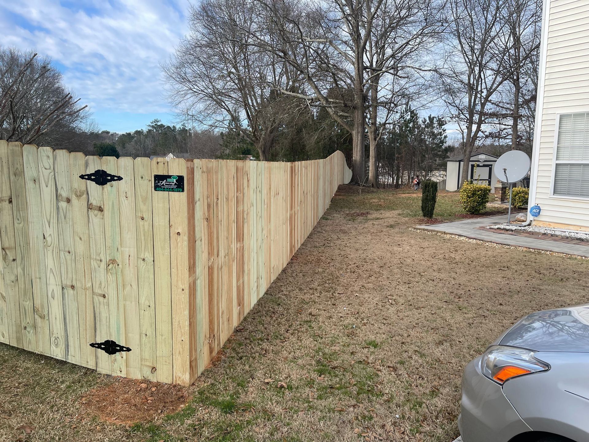 Wooden privacy fence along a gravel side yard beside a house and parked car