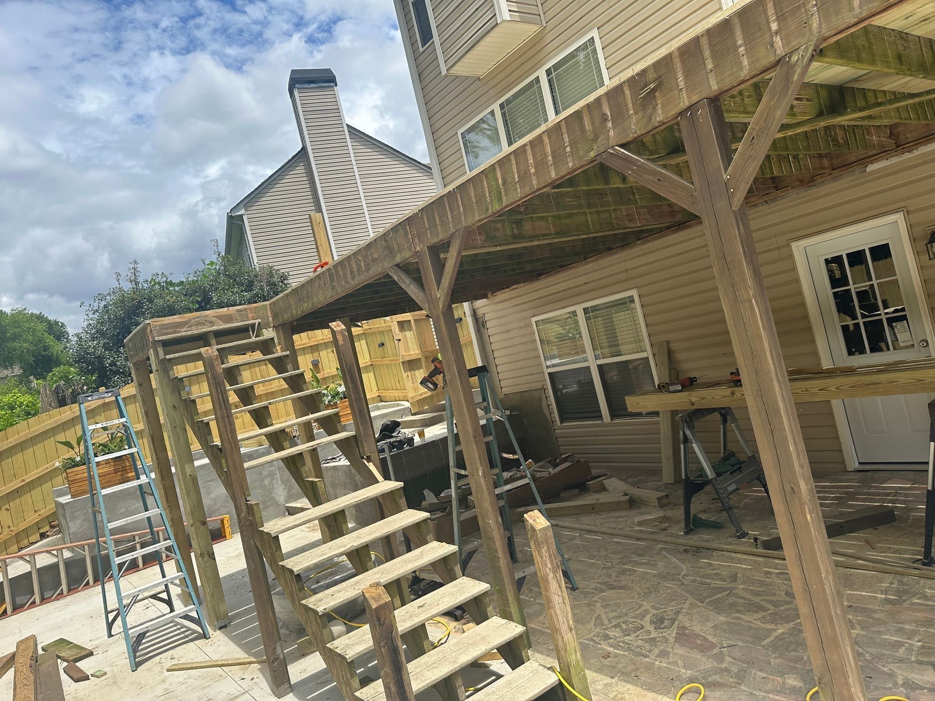 Backyard deck under construction with wooden stairs, posts, and scaffolding beside a house