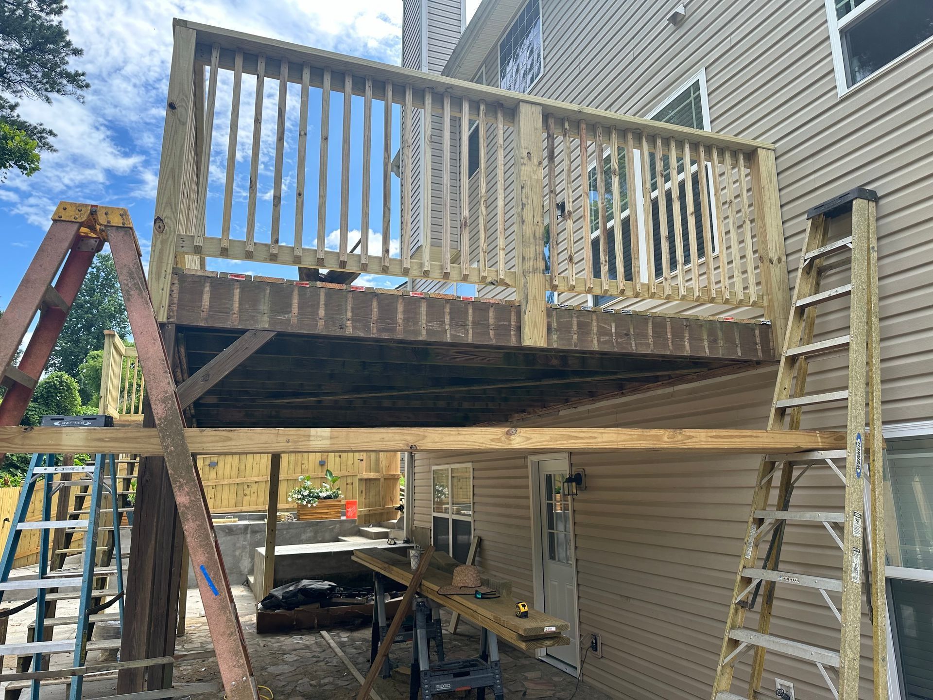 Backyard deck under construction beside a house, with ladder, railing, and support beams