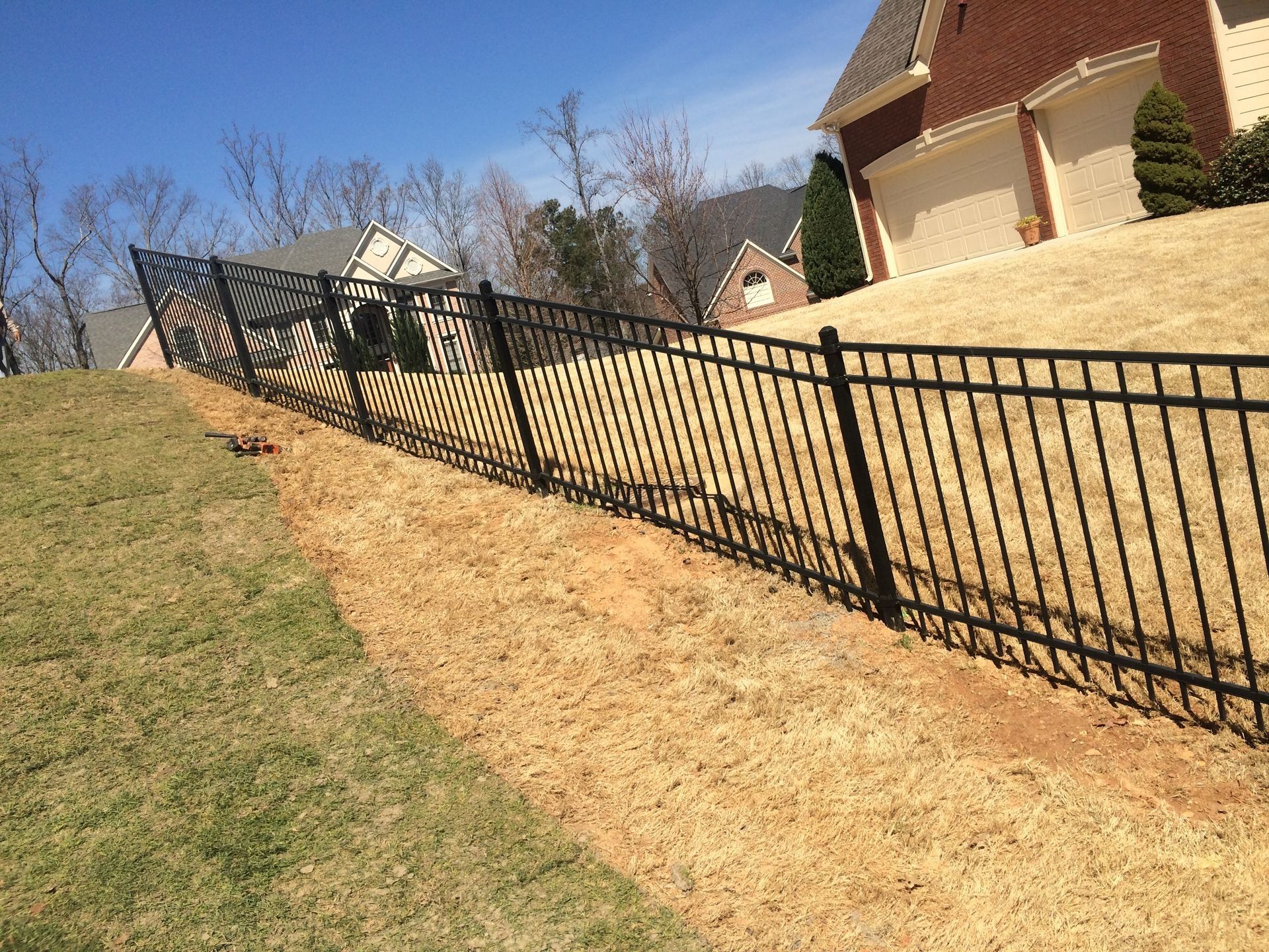 Black metal fence along a sloped yard beside a brick house on a sunny day