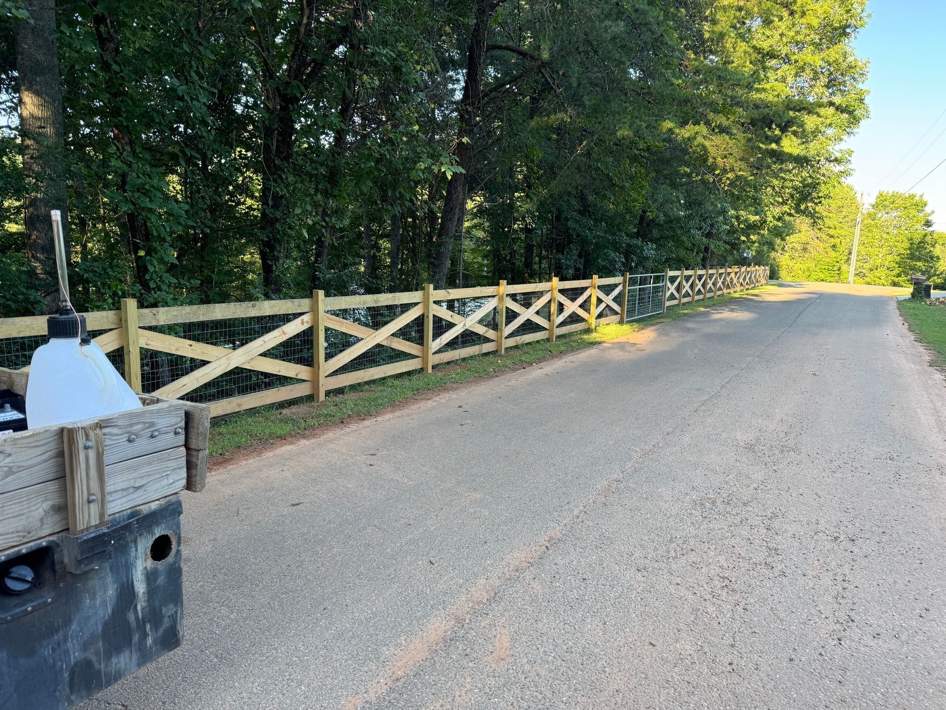 Gravel road beside a wooden fence and trees in bright sunlight