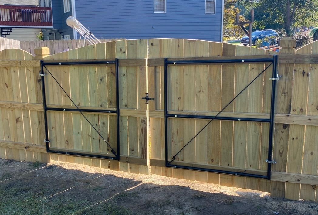 Wooden double gate with black metal braces on a fenced backyard, with a blue house behind it.