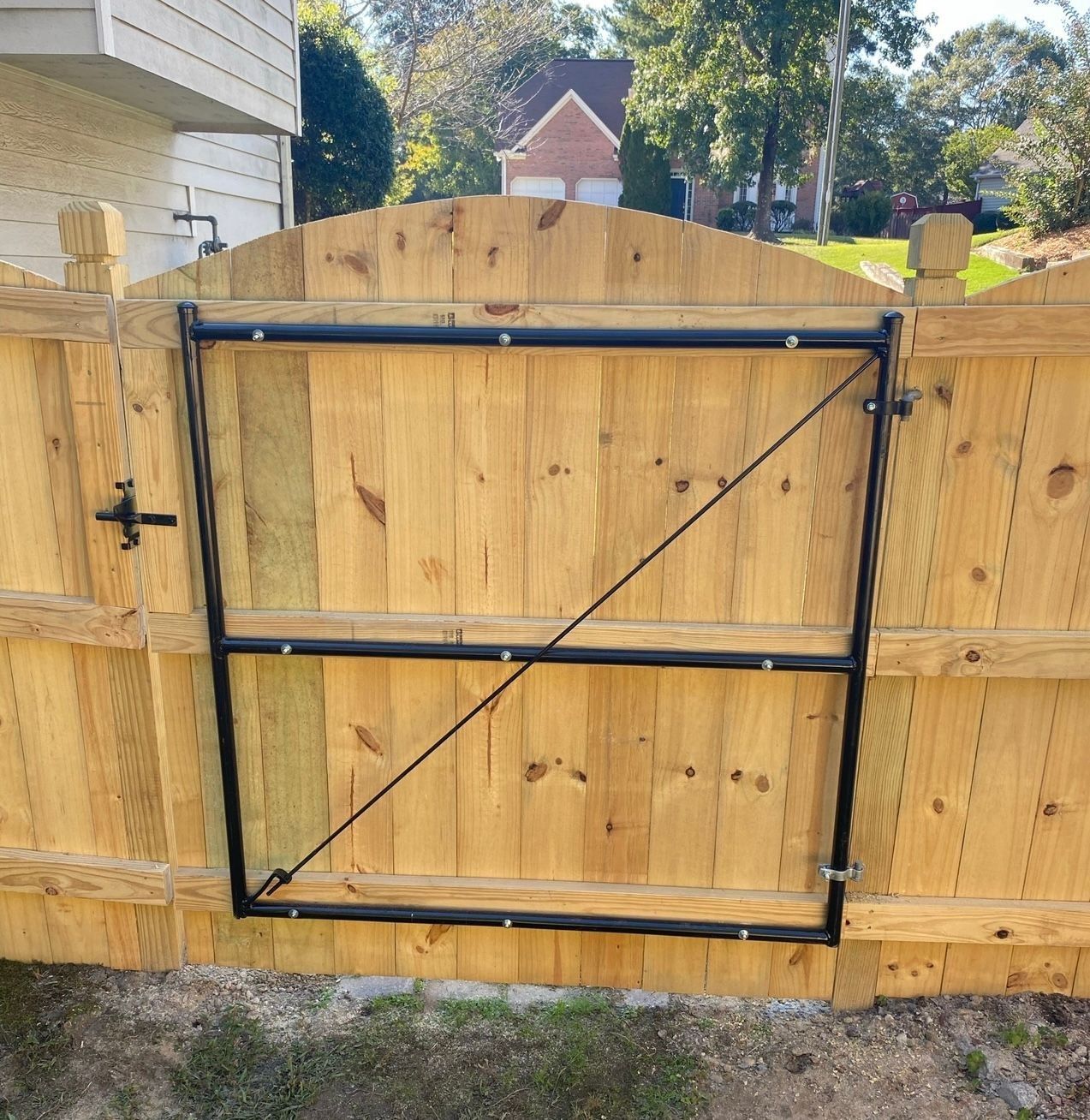 Black metal gate installed in a wooden privacy fence in a sunny backyard