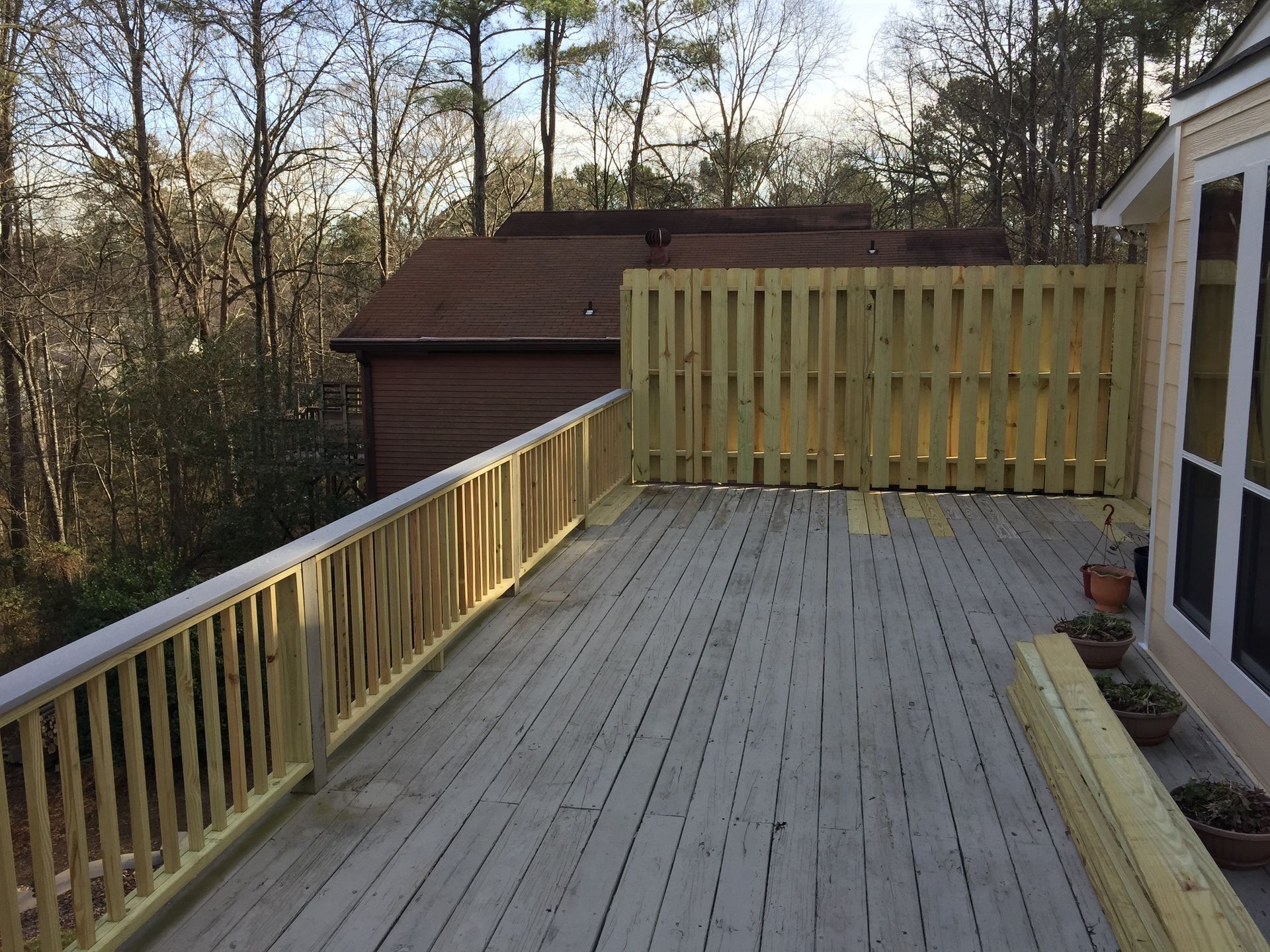 Wooden deck with railing overlooking a wooded backyard beside a house and shed.