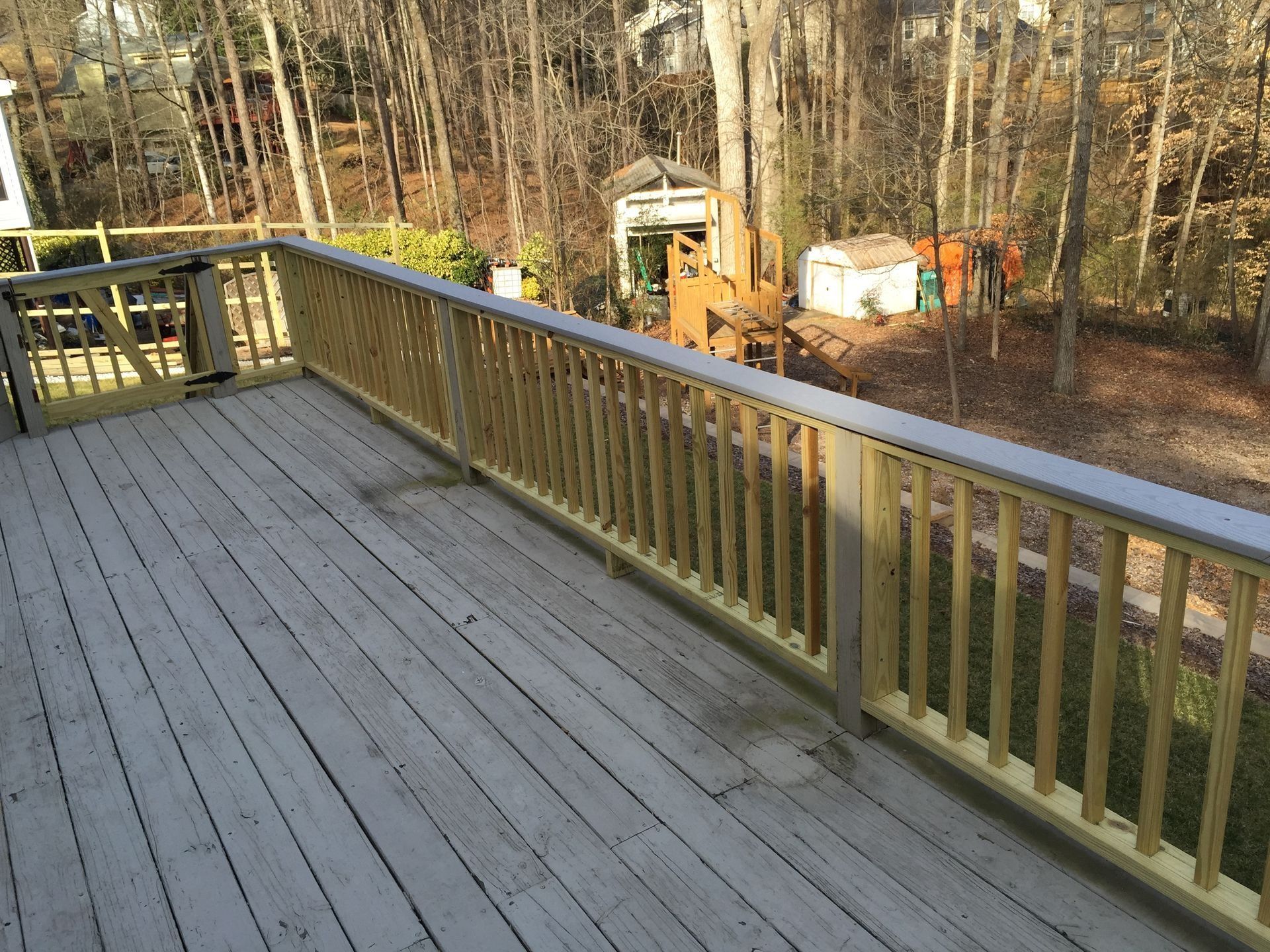 Wooden deck with railing overlooking a wooded yard and construction equipment beyond.