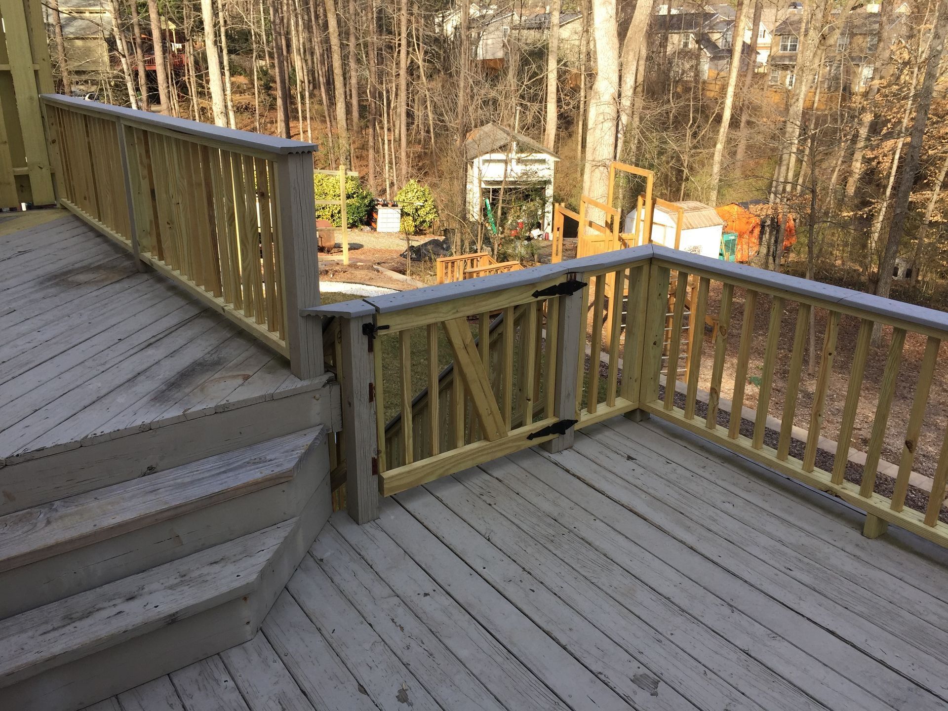 Wooden deck and stairs with railing overlooking a backyard garden in daylight