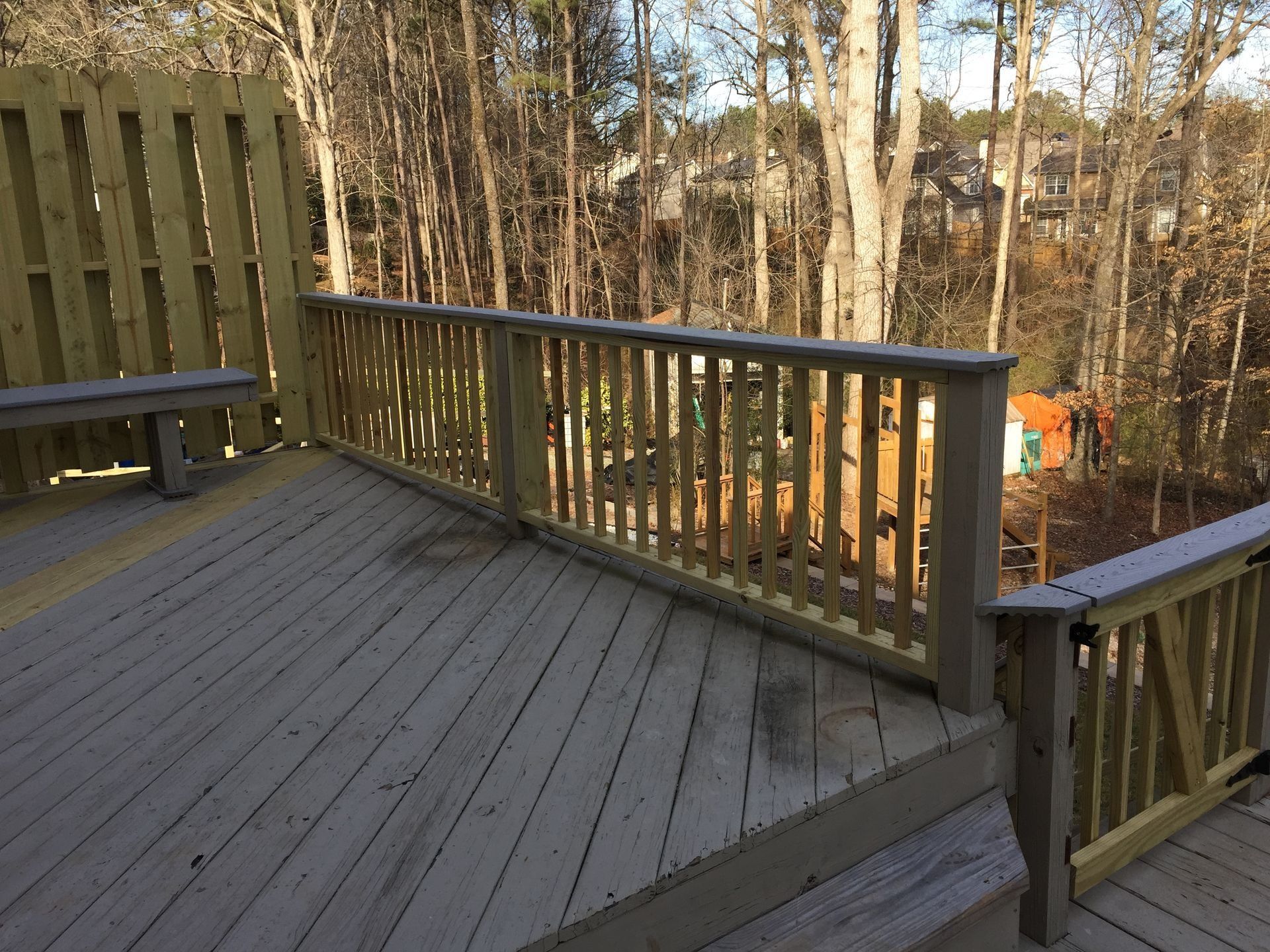 Wooden deck with railings overlooking a wooded yard in warm daylight