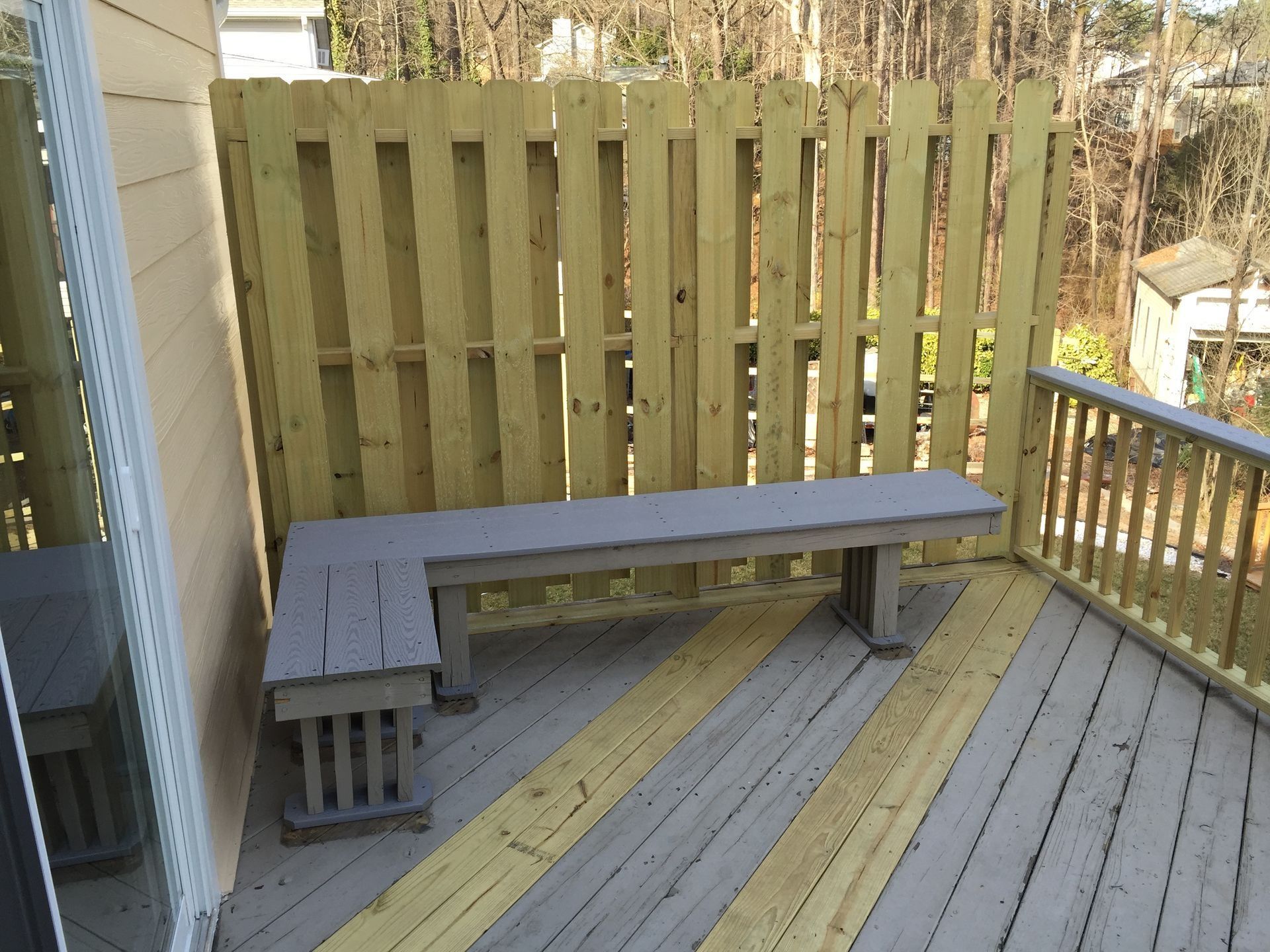 Wooden outdoor bench on a sunlit deck beside a tall privacy fence