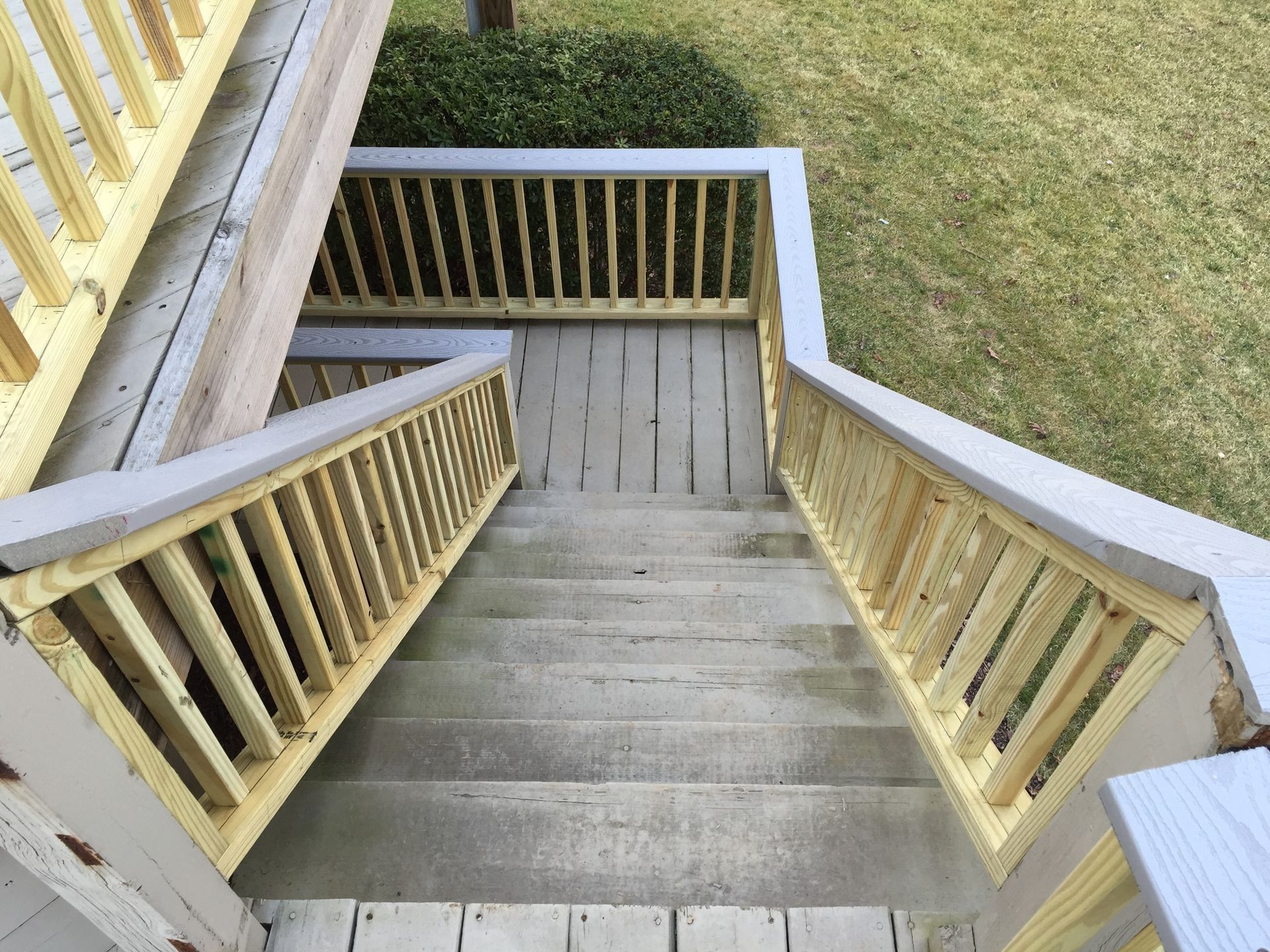 Wooden outdoor staircase descending to a small landing, viewed from above with grassy yard beside it.