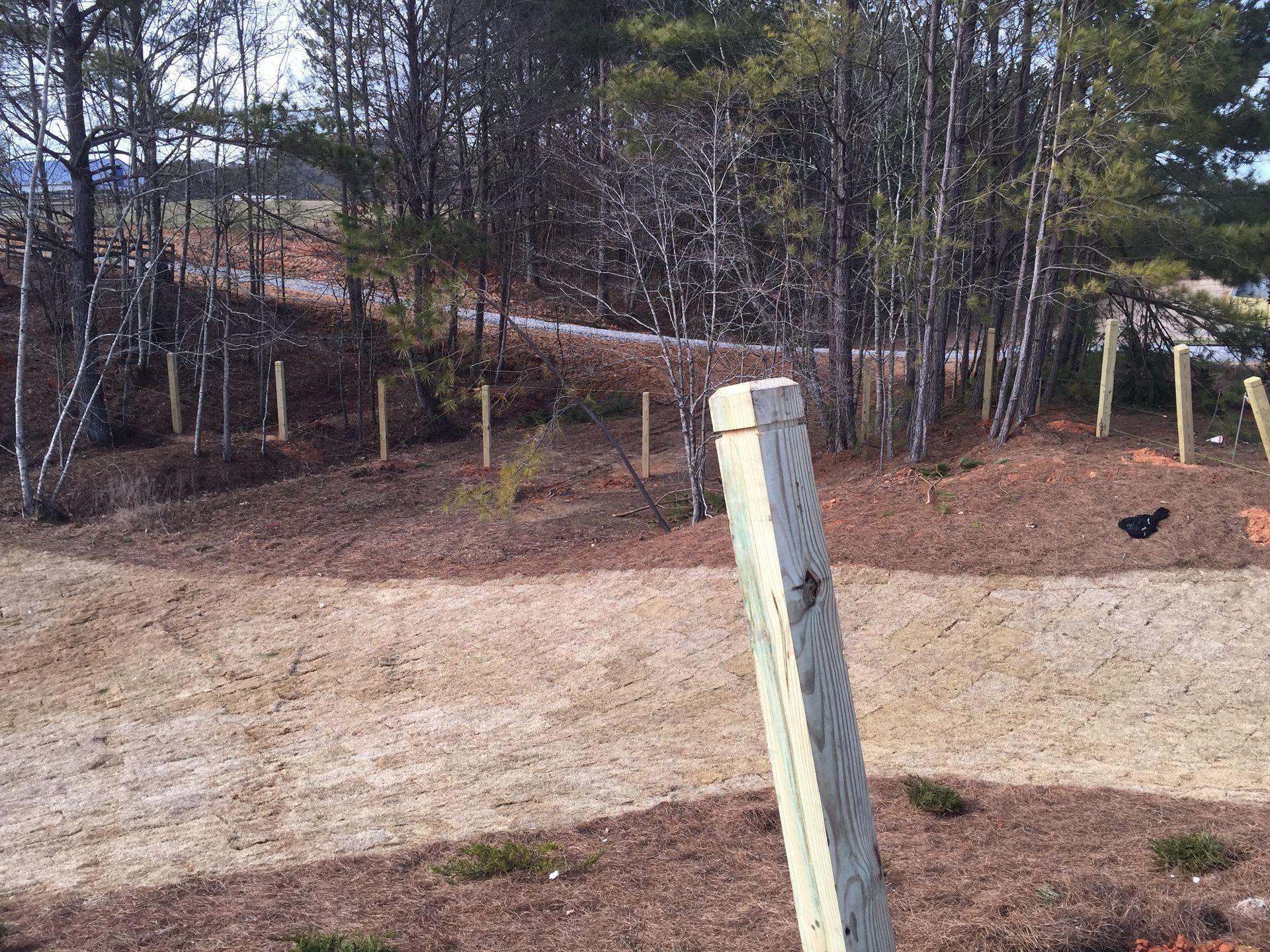 Gravel lot beside a wooded area, with a leaning white post in the foreground.