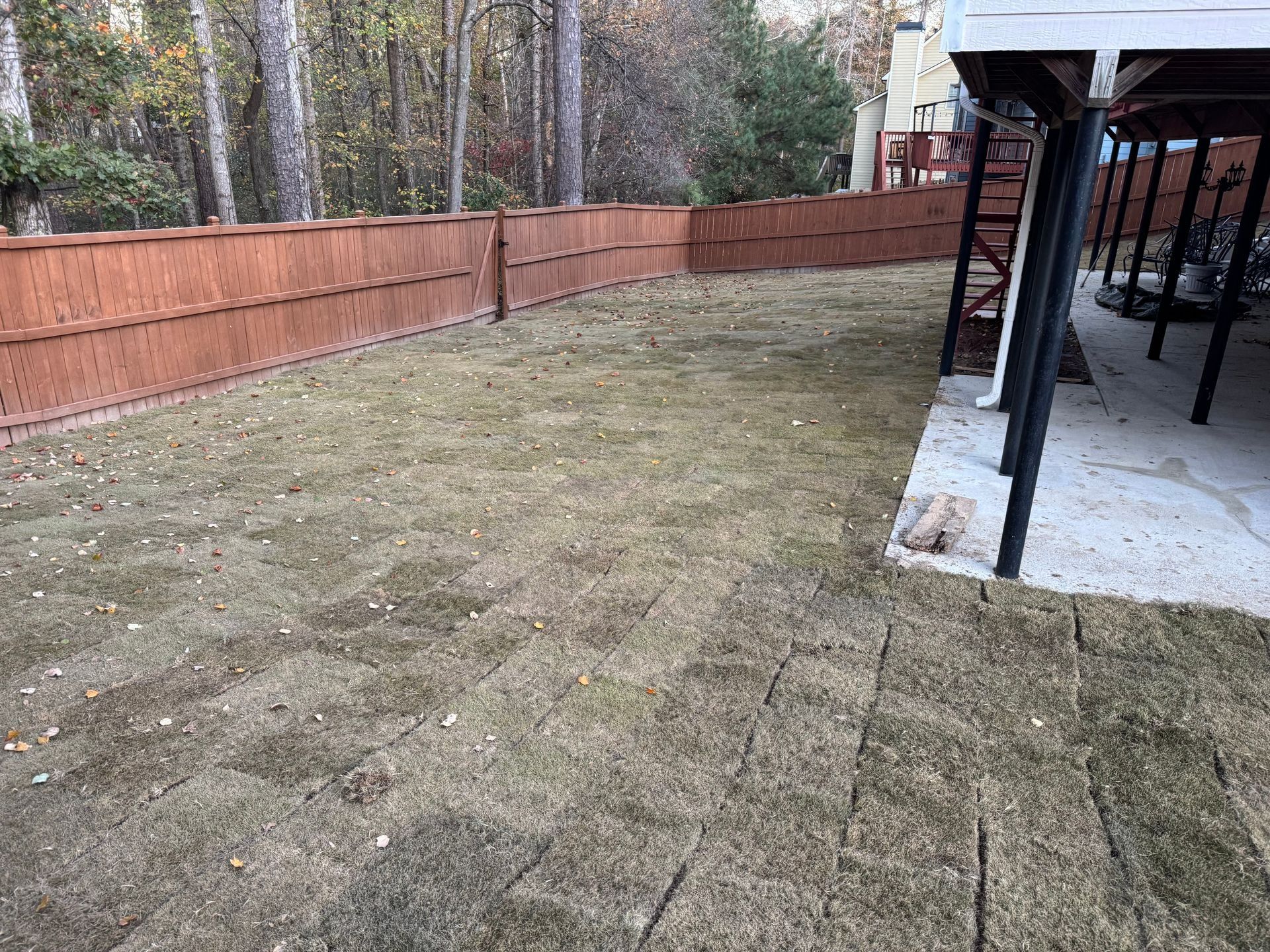 Backyard with patchy grass, a wooden fence, and a covered patio on the right.