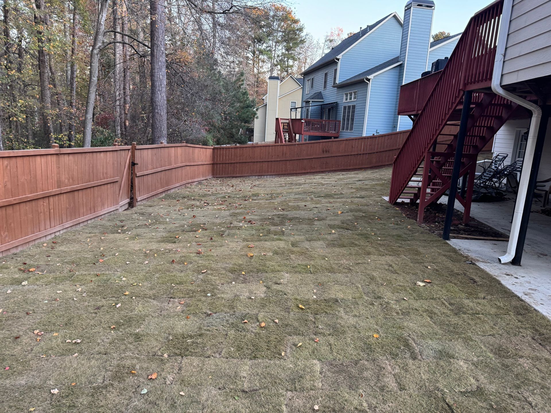 Backyard with fenced lawn and red deck stairs beside a house