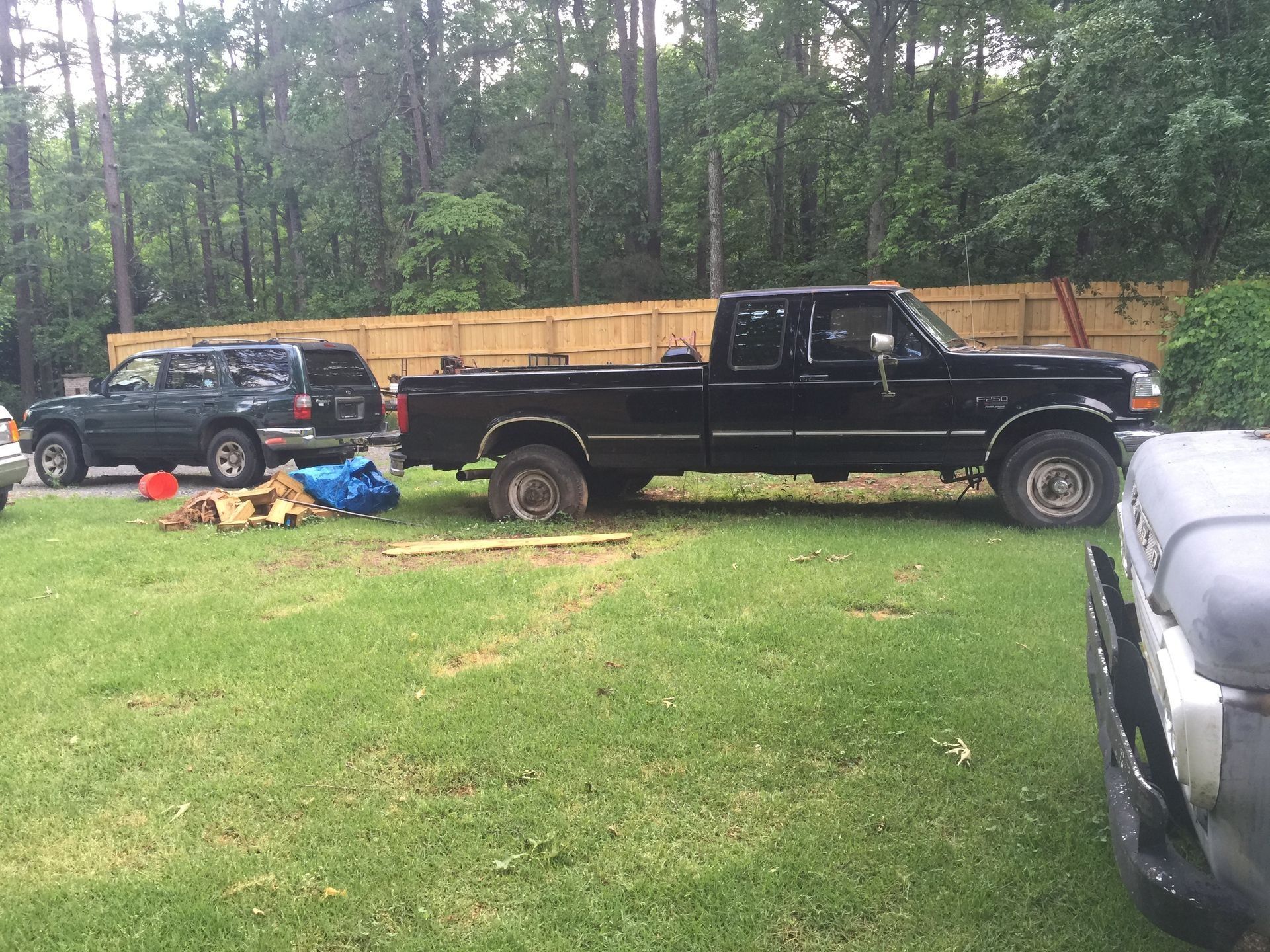 Black pickup truck parked on grass beside an SUV and debris, with a wooded area in the background
