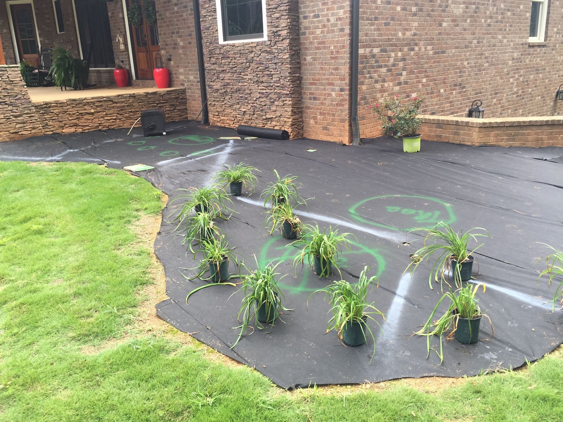 Newly planted garden bed covered with black mulch beside a brick house and green lawn