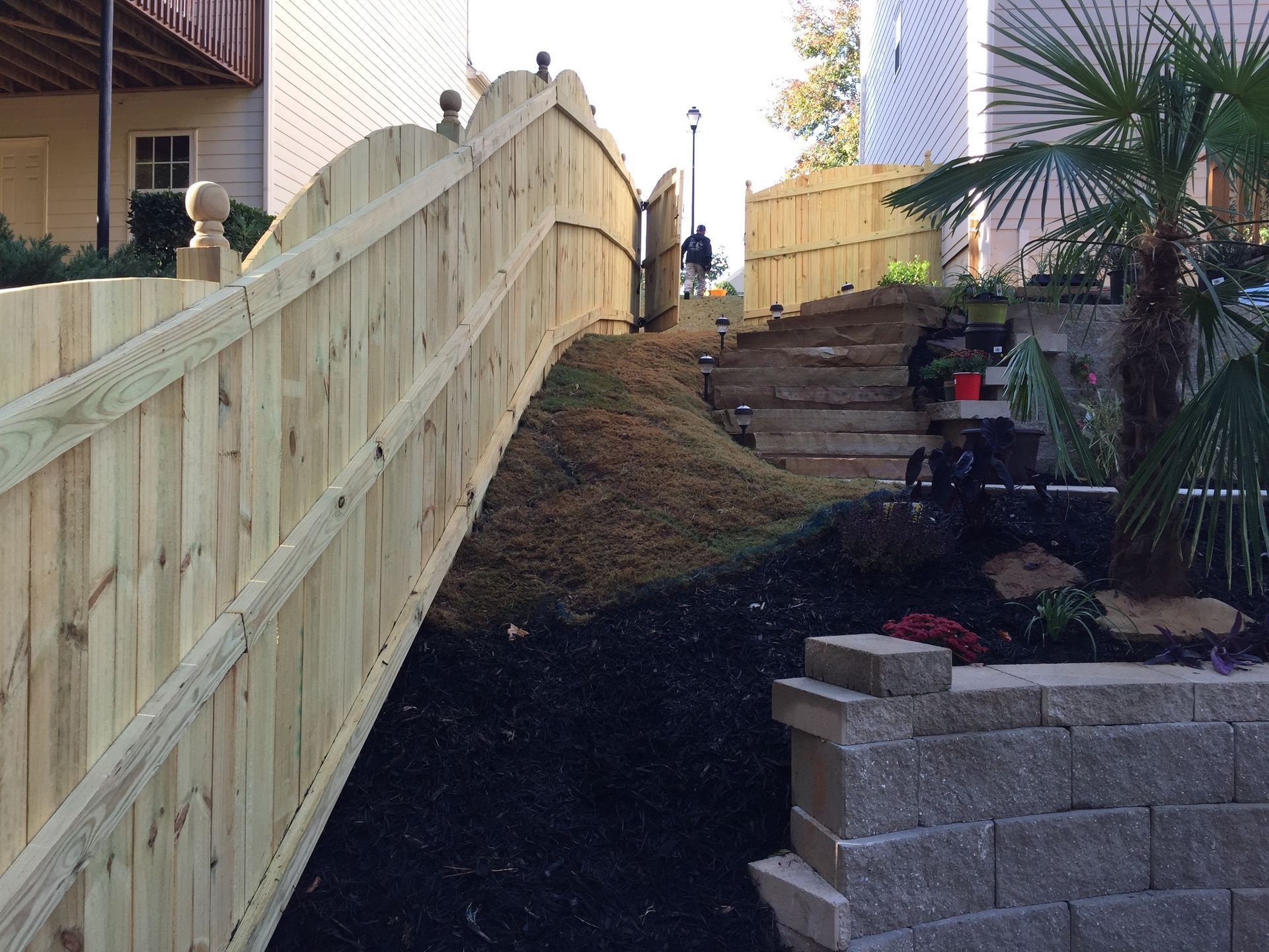 Wooden fence beside a landscaped sloped walkway with stone steps and a retaining wall