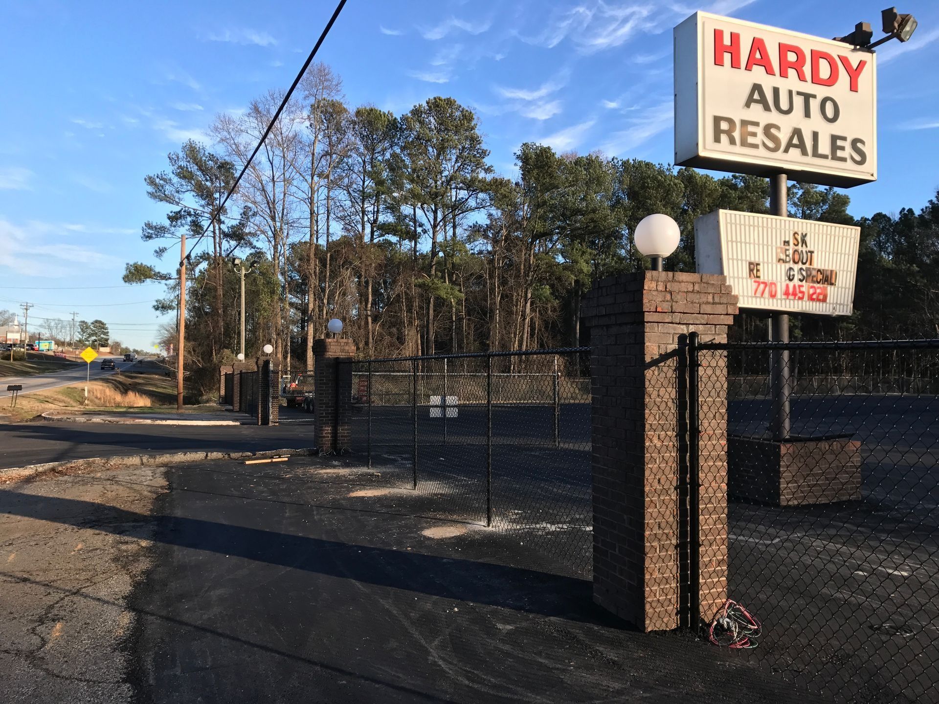 Hardy Auto Resales roadside sign and gated lot on a sunny street