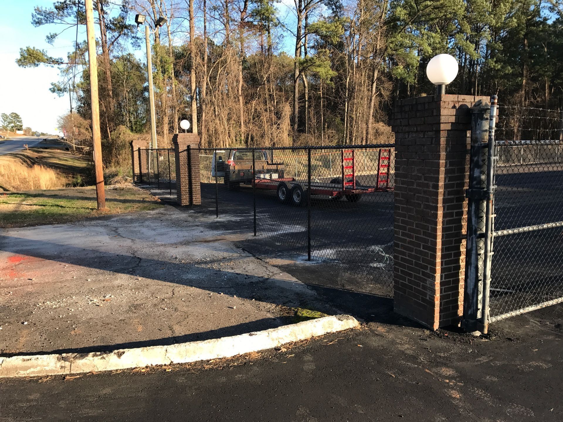 Gated driveway entrance with black fence, brick pillars, and trees in the background