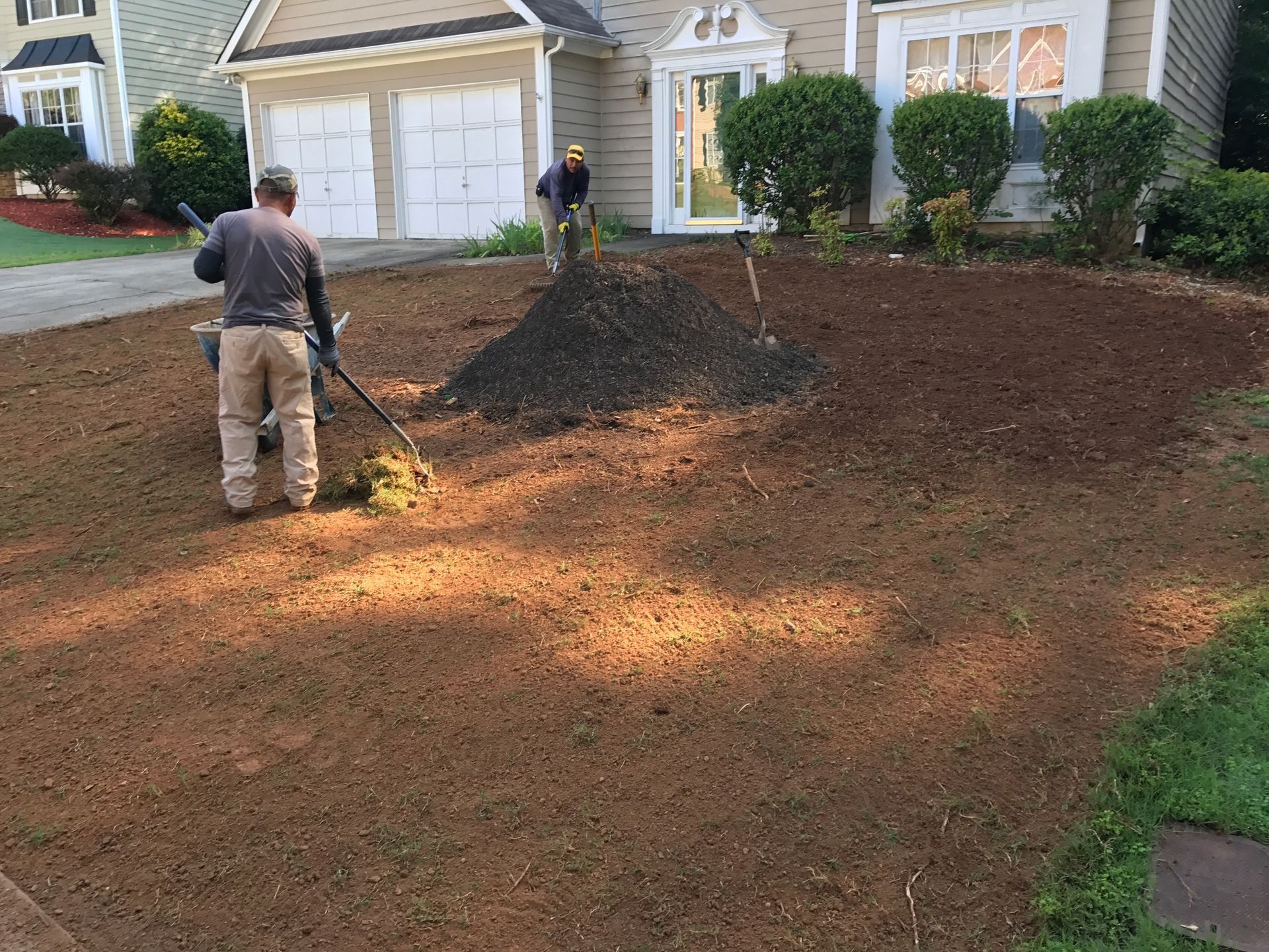 Workers spreading mulch across a front yard in front of a suburban house