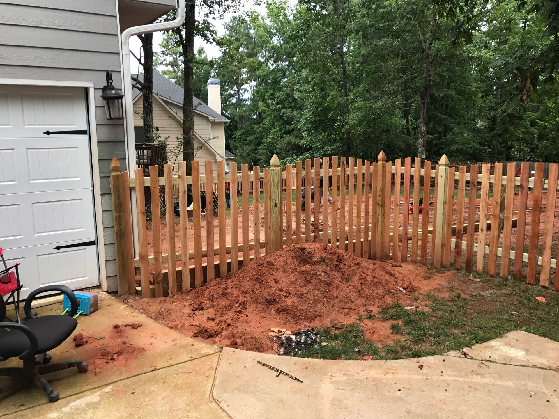 Backyard fence with a mound of red dirt beside a garage and patio area