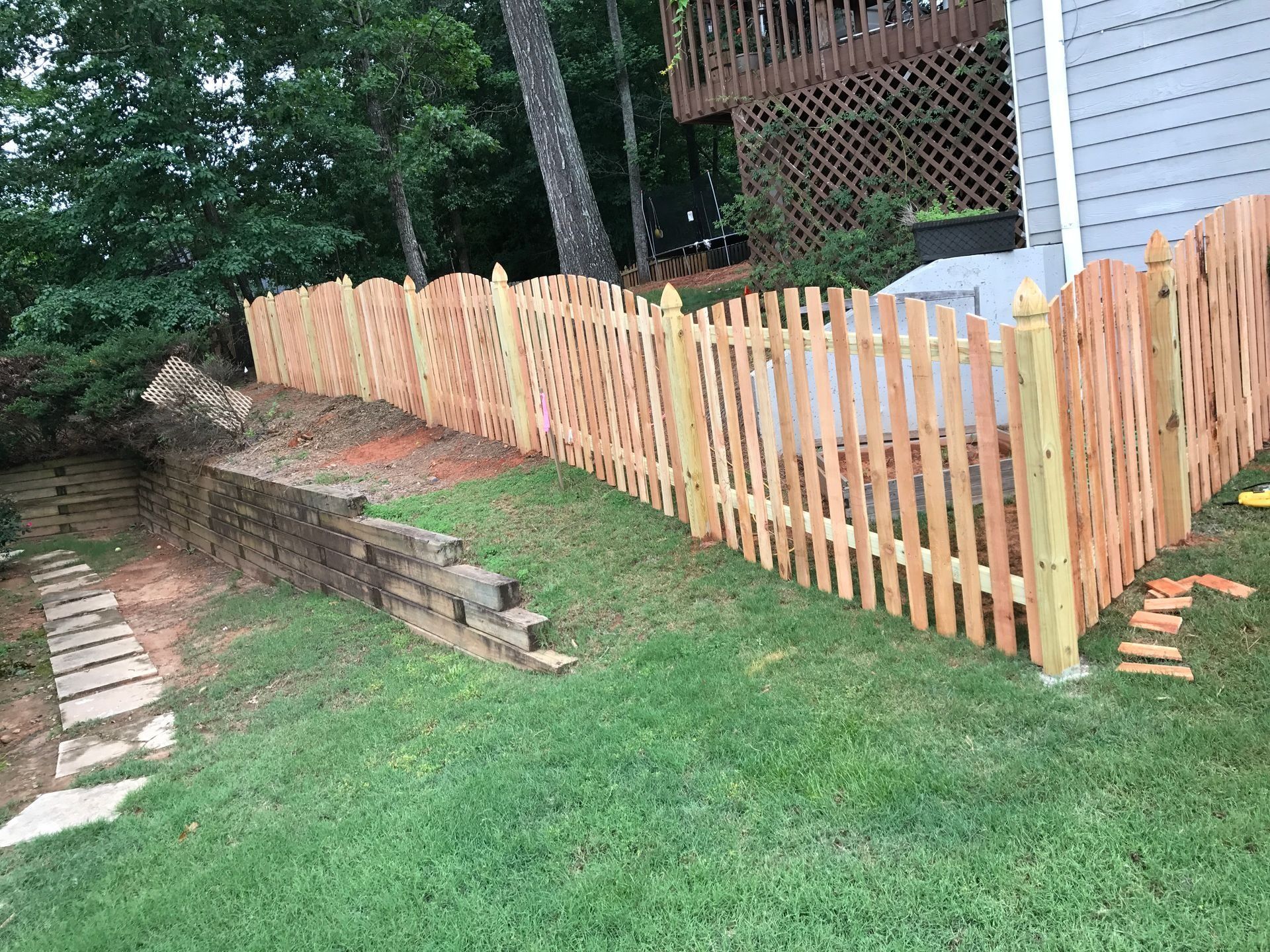 Wooden picket fence along a grassy yard beside steps and a house in a wooded area