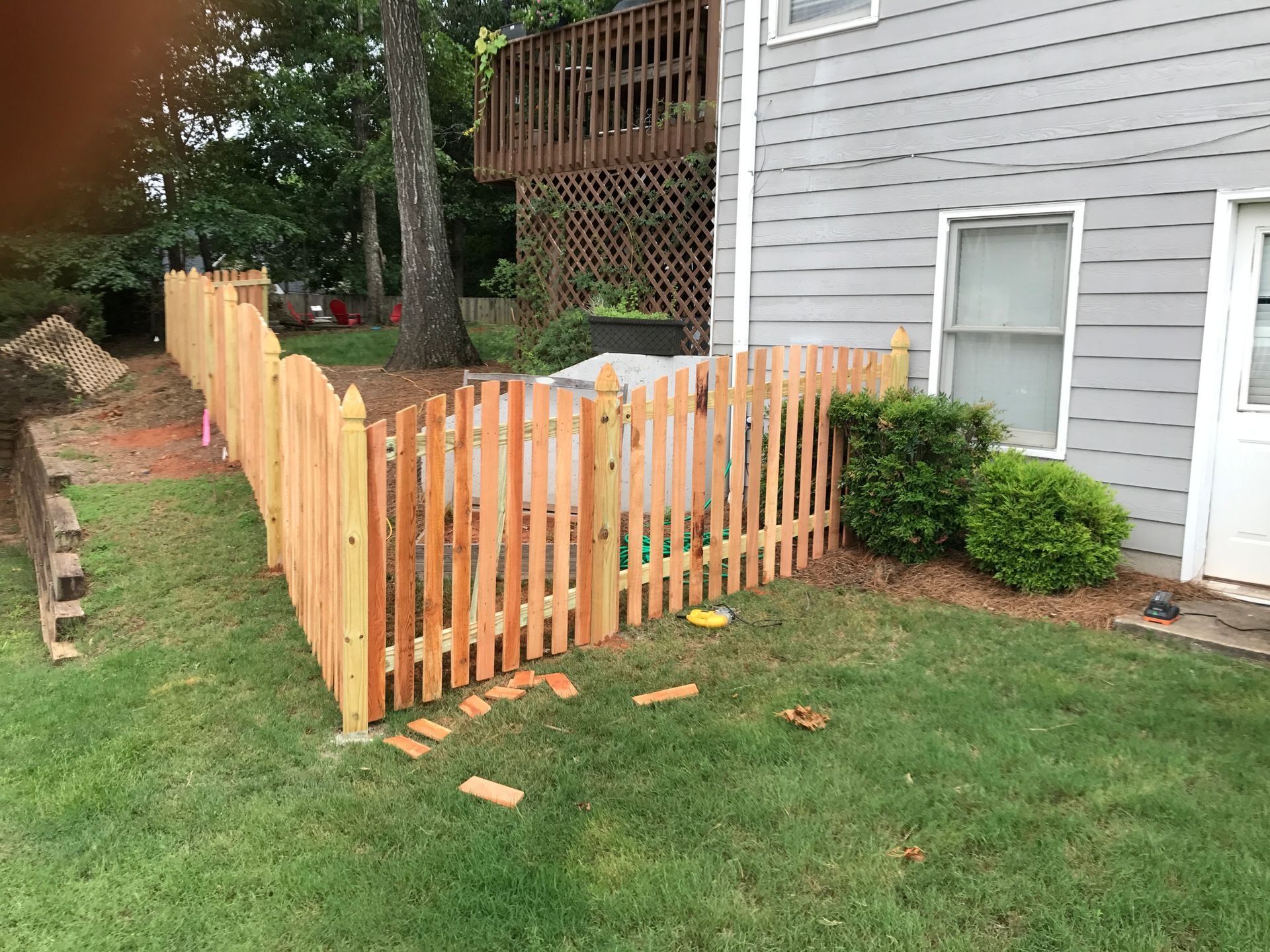 New light wood picket fence around a yard beside a gray house