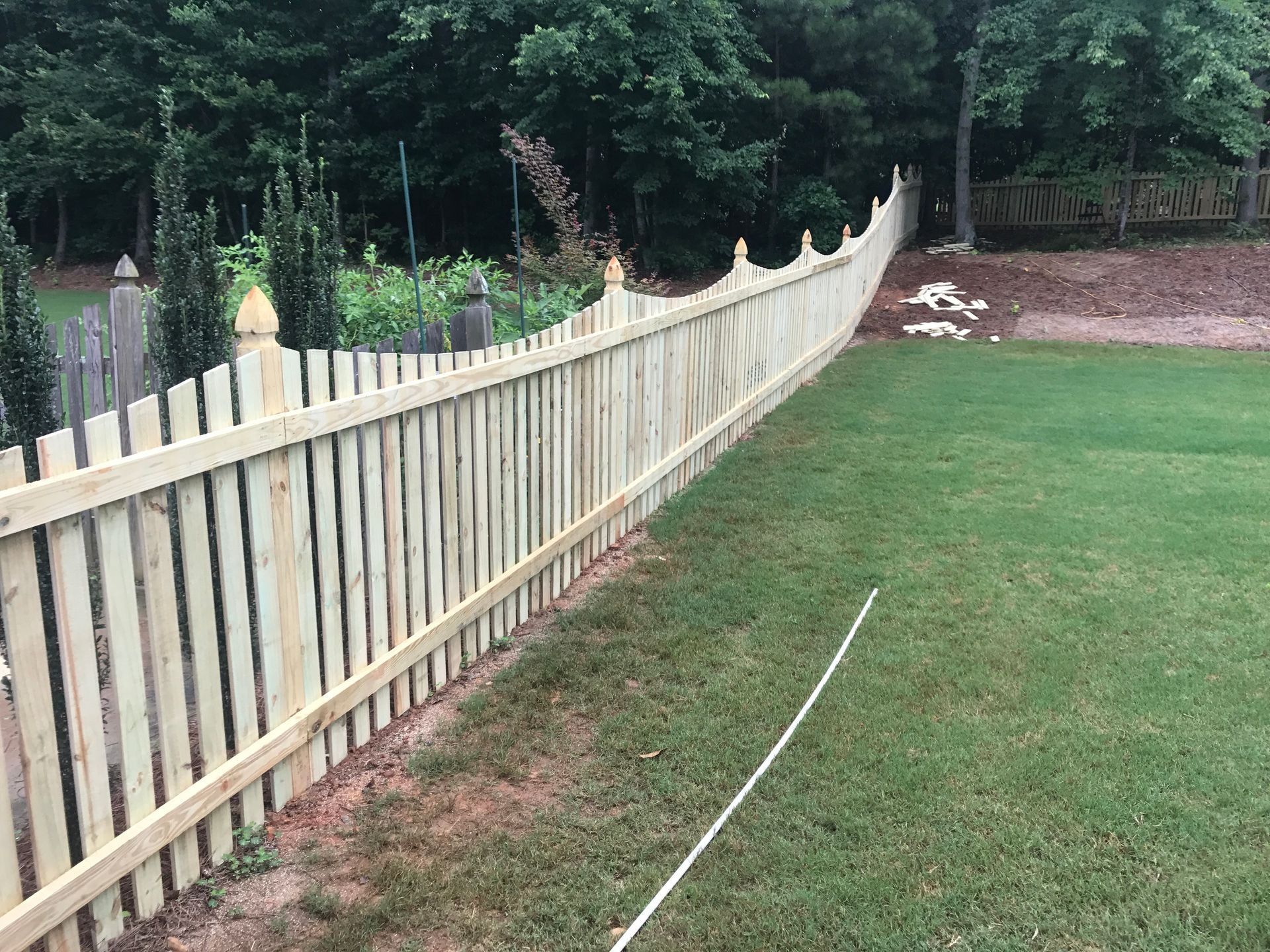 Wooden picket fence lining a green lawn beside trees and a garden bed