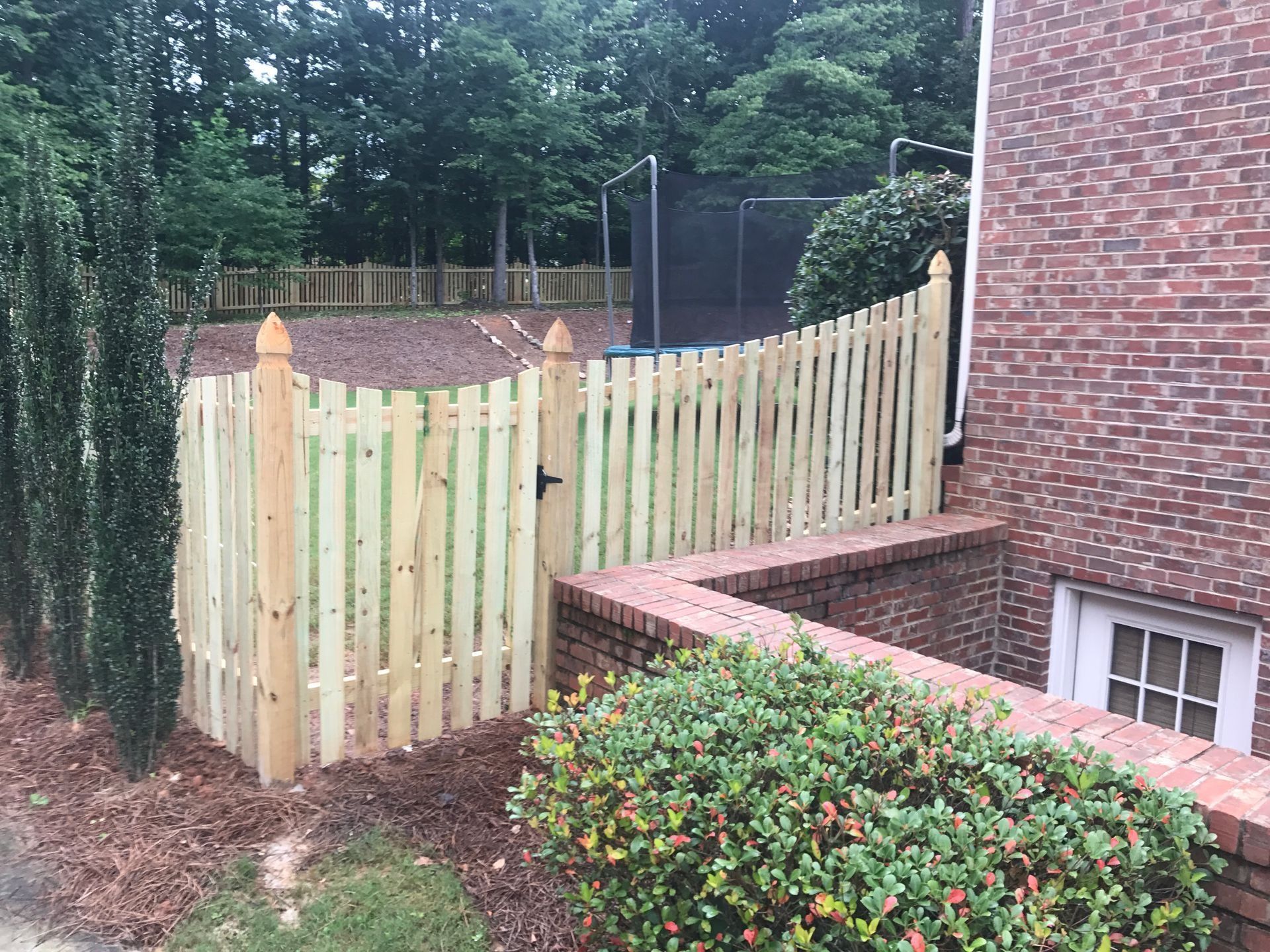 Wooden fence along a brick house beside a leafy garden and trees