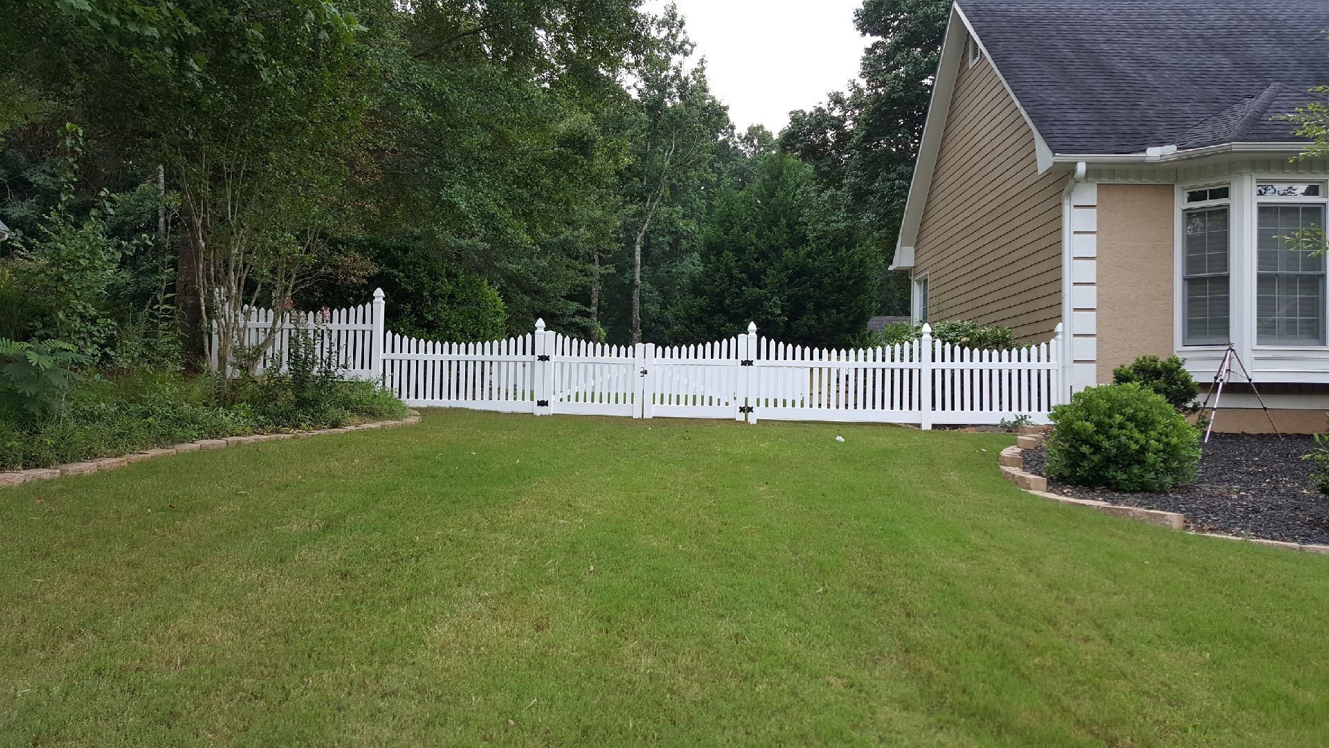 Green lawn beside a white picket fence and brick house in a suburban yard