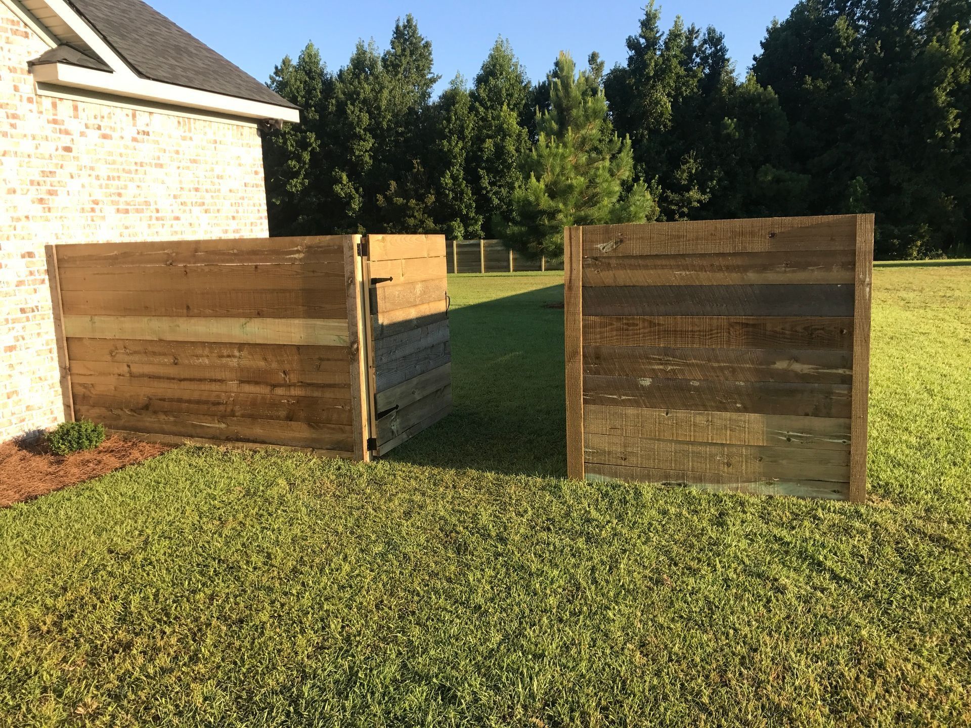 Two wooden raised garden beds on a grassy lawn beside a house, with trees in the background